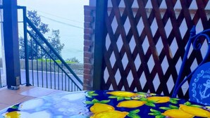 Une pièce avec une table recouverte d’une nappe à motifs bleus et jaunes, un seau en métal et une porte à treillis.