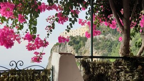 Un bâtiment à la façade en pierre, entouré d’une végétation luxuriante et orné de fleurs de bougainvillier roses.