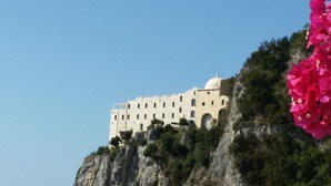 Un grand bâtiment doté de nombreuses fenêtres et d’un dôme, situé sur une falaise rocheuse et entouré de verdure.