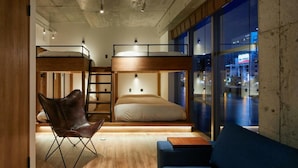 Ein modernes Zimmer mit Etagenbetten, einem Klappstuhl, einer Couch und Blick auf die nächtliche Stadt.