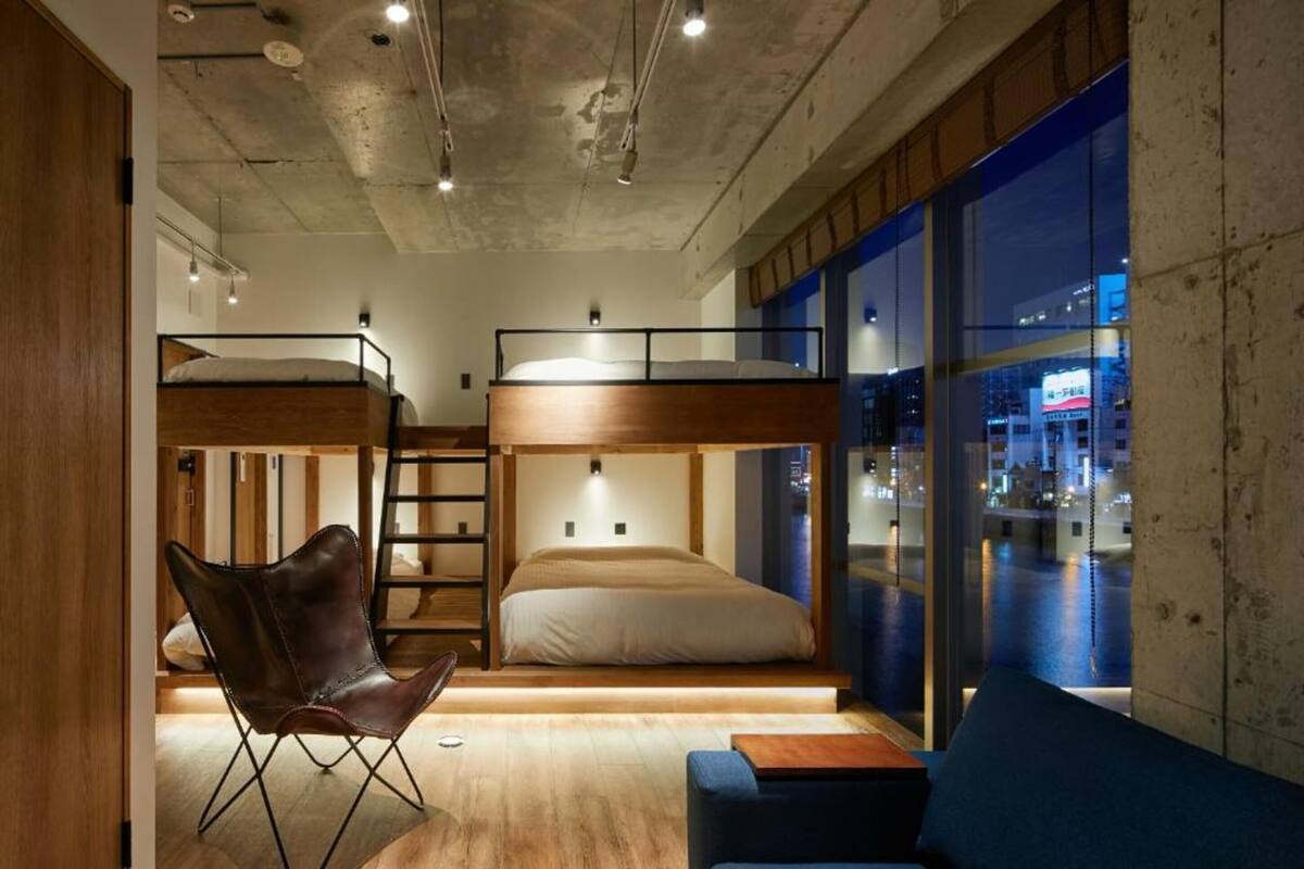 Ein modernes Zimmer mit Etagenbetten, einem Klappstuhl, einer Couch und Blick auf die nächtliche Stadt.