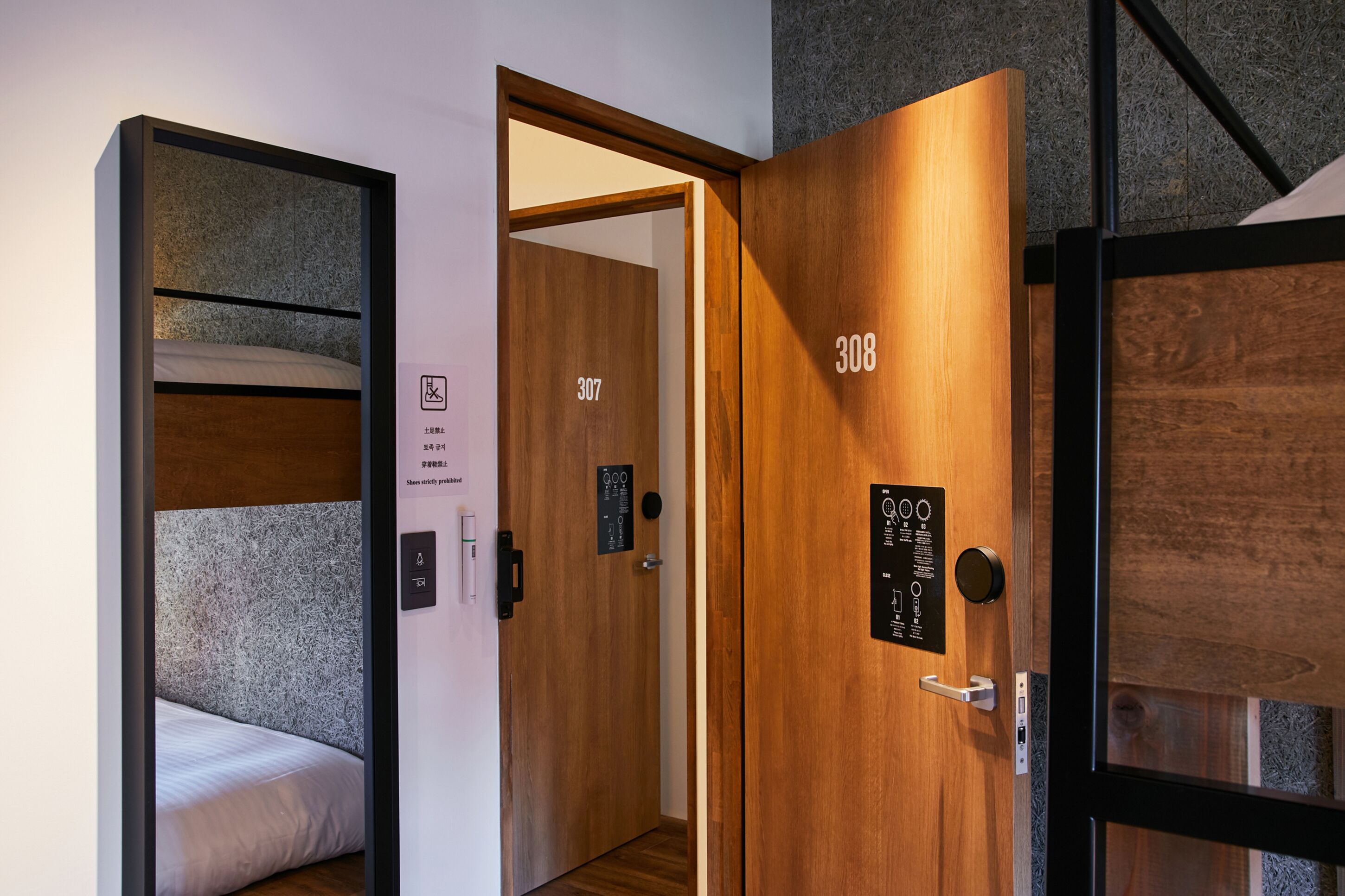Une chambre d’hôtel avec un lit, une porte en bois portant le numéro de la chambre, et une vue sur une autre chambre.