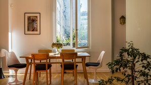 A dining area with a table and chairs, a window with a view of buildings, and a potted plant. - The Library Wall, by Veeve (Paris)