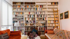 A room with two orange sofas, a marble coffee table with a vase, and a large bookshelf filled with books. - The Library Wall, by Veeve (Paris)