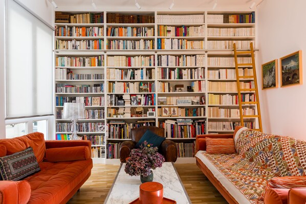 A room with two orange sofas, a marble coffee table with a vase, and a large bookshelf filled with books. - The Library Wall, by Veeve (Paris)