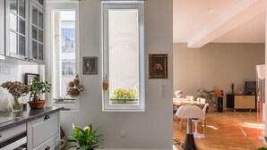 A modern kitchen with a large window, a dining area with a table and chairs, and a living room with a sofa and a lamp. - The Library Wall, by Veeve (Paris)