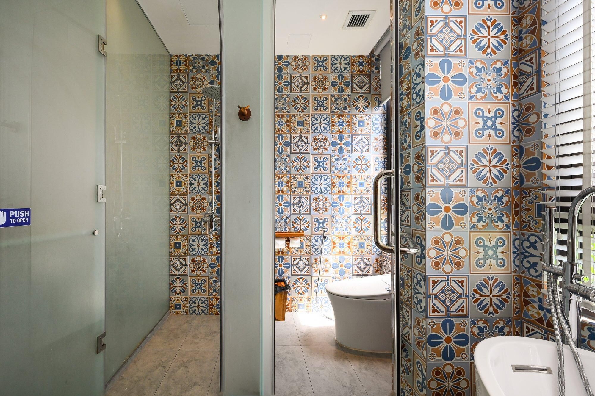 A bathroom with a glass door, patterned tiles, a toilet, and a shower area.