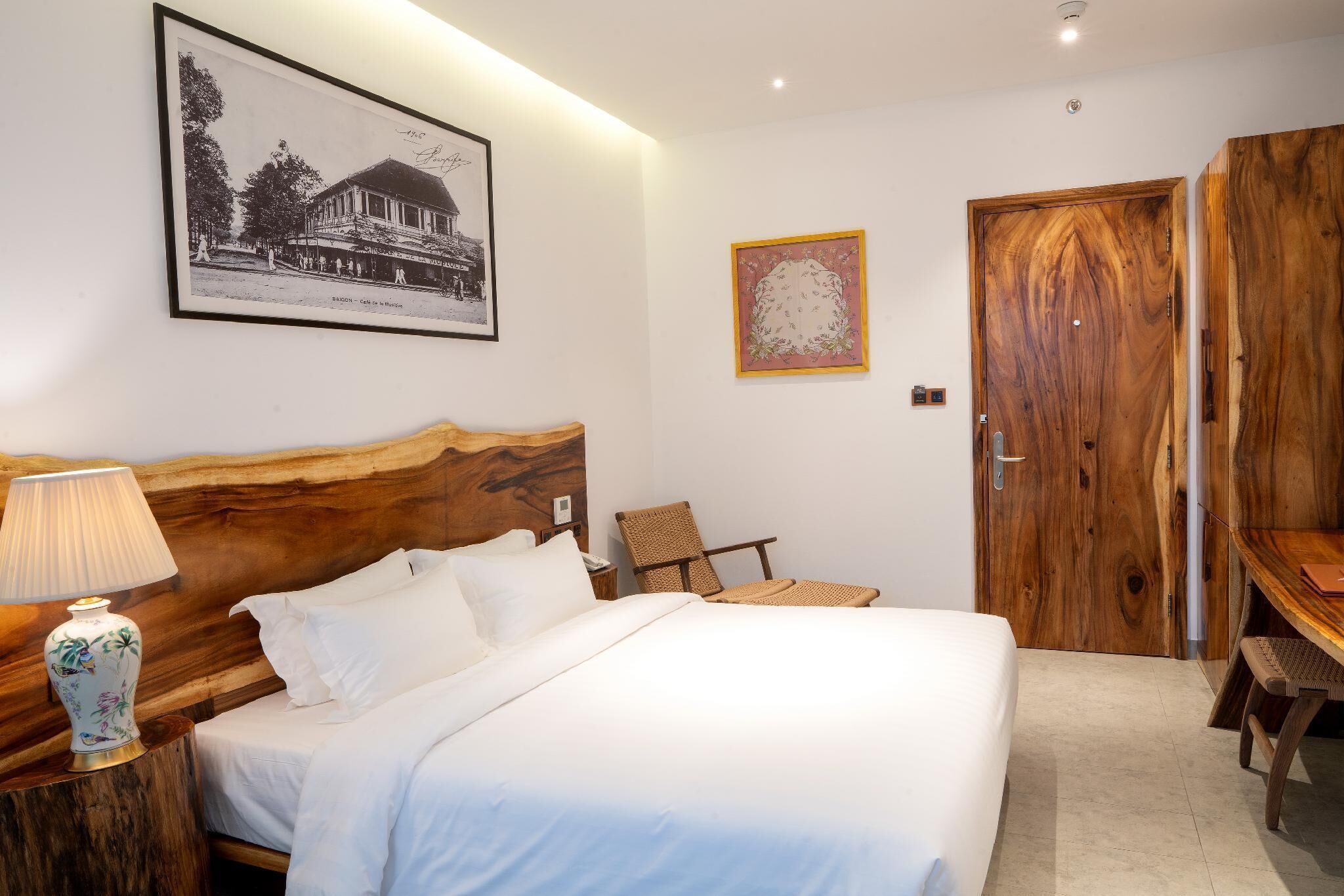 A neatly arranged bedroom with a large bed, a wooden headboard, a chair, a table, and a framed picture on the wall.