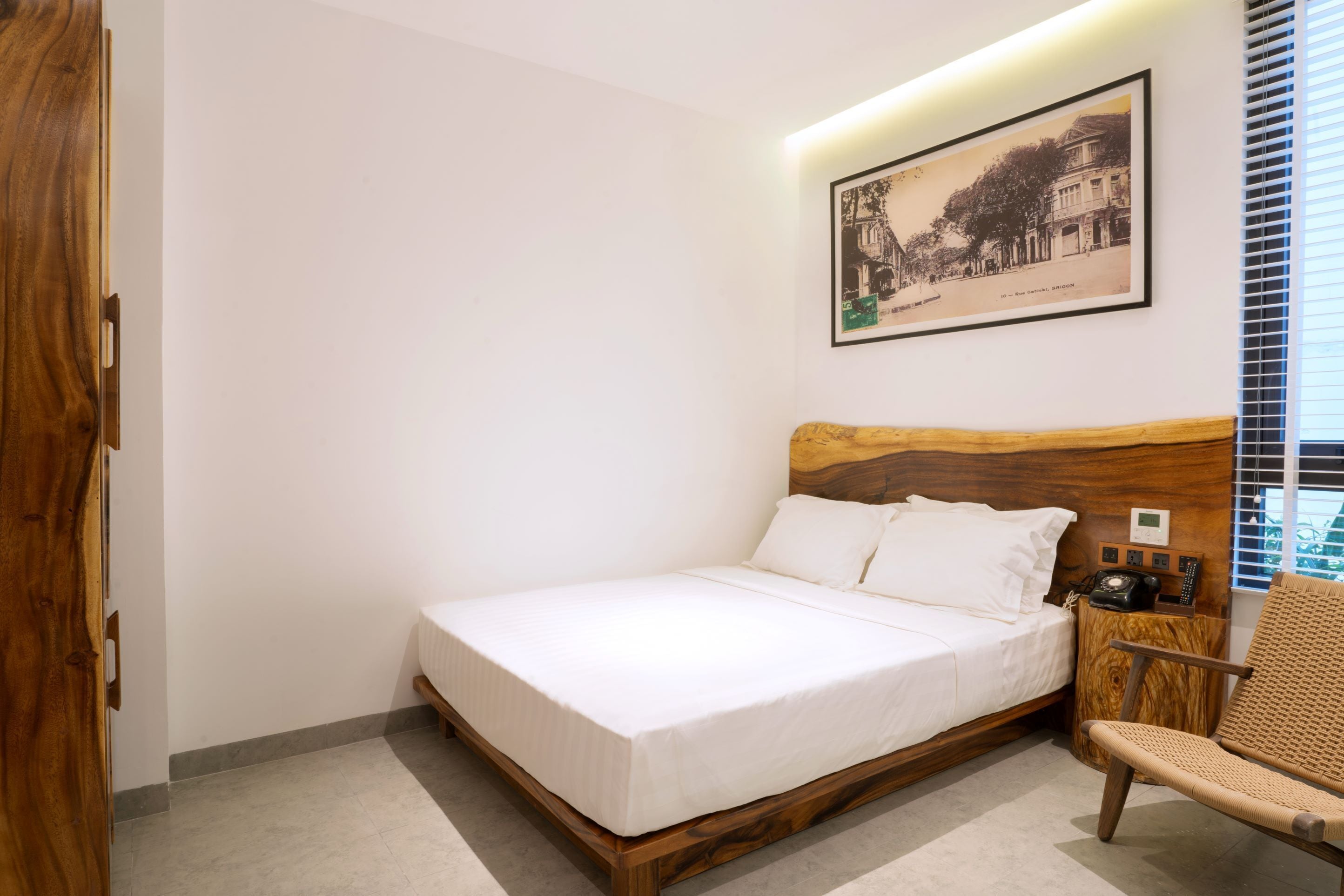 A neatly made bed with a wooden headboard, a small bedside table with a telephone, and a framed picture on the wall.