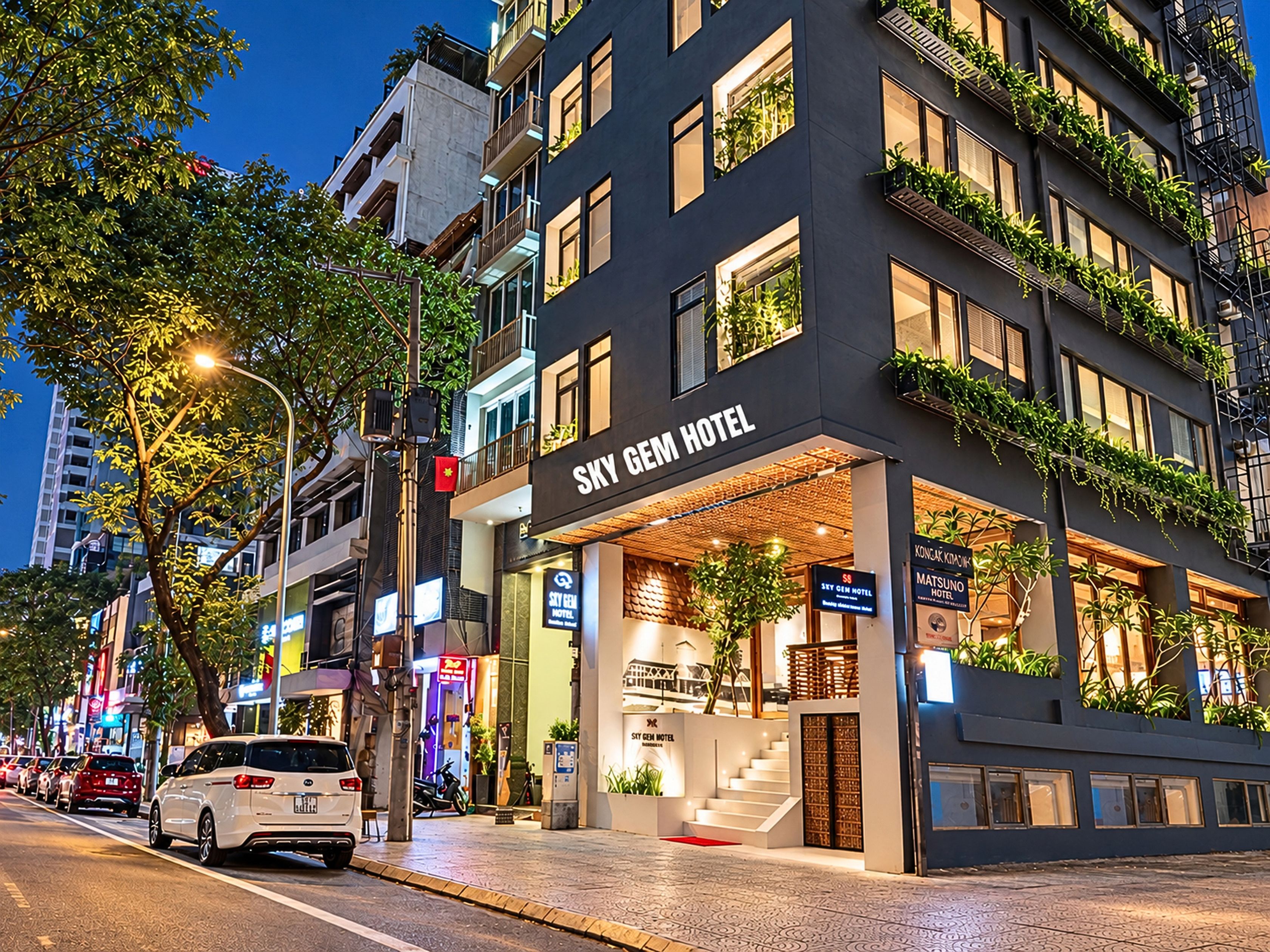 Un hotel con una fachada moderna, varios balcones con plantas y una entrada visible.