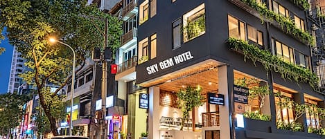 Un hotel con una fachada moderna, varios balcones con plantas y una entrada visible.