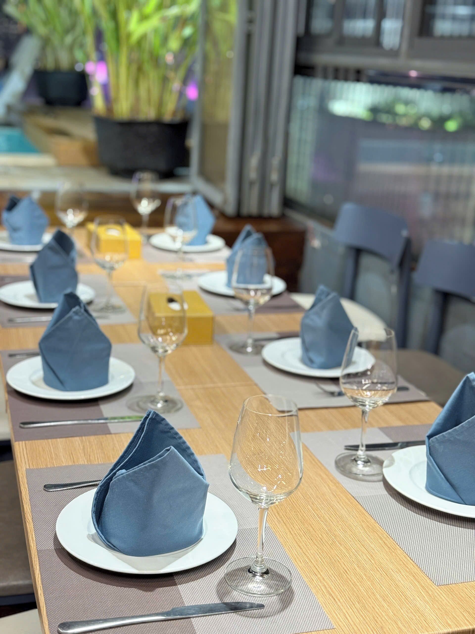 Une table à manger dressée avec des assiettes, des serviettes et des verres à vin.