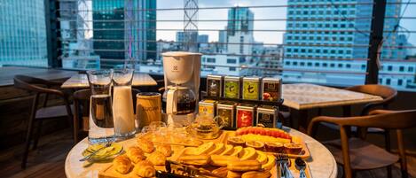 Una mesa con pasteles, té y café en un restaurante con vistas a la ciudad.