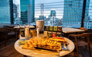 Uma mesa com doces, chá e café em um restaurante com vista para a cidade.