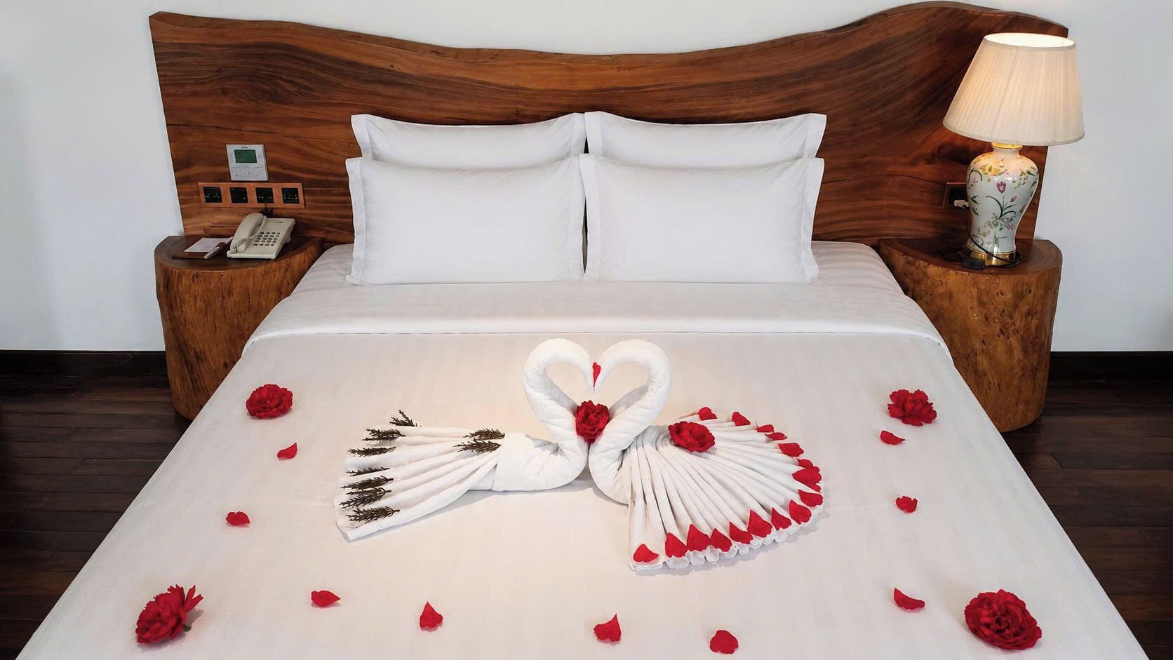 A neatly made bed with a swan and rose decoration, a wooden headboard, bedside tables with lamps, and a telephone.