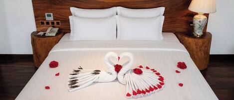 A neatly made bed with a swan and rose decoration, a wooden headboard, bedside tables with lamps, and a telephone.