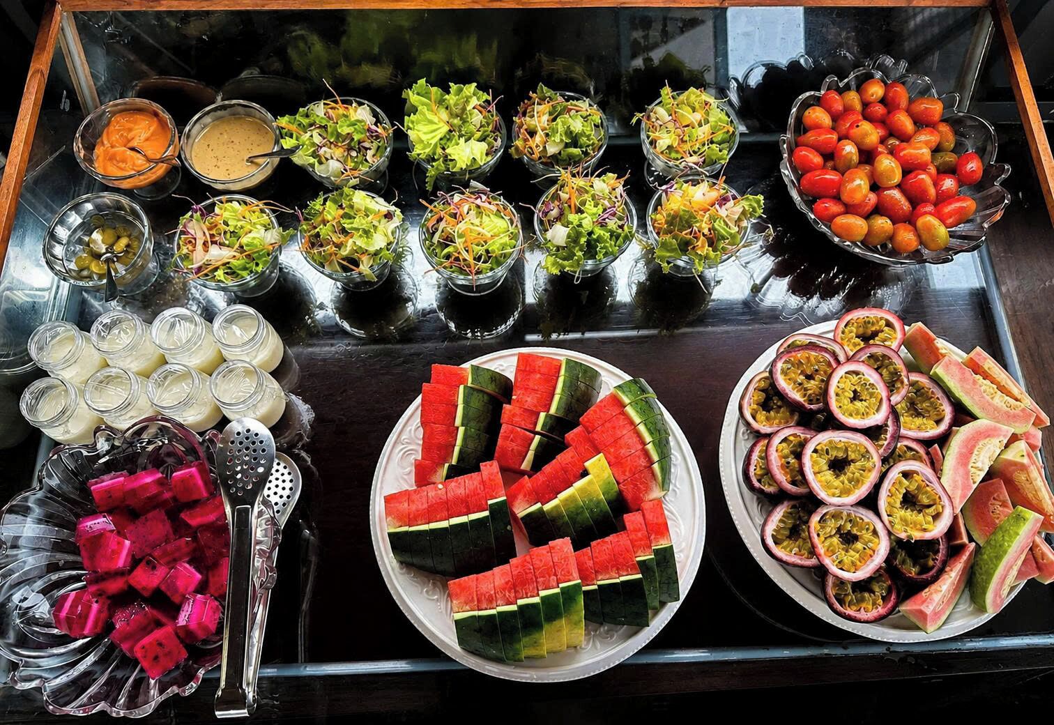 A buffet with various food items including watermelon, passion fruit, and salads.