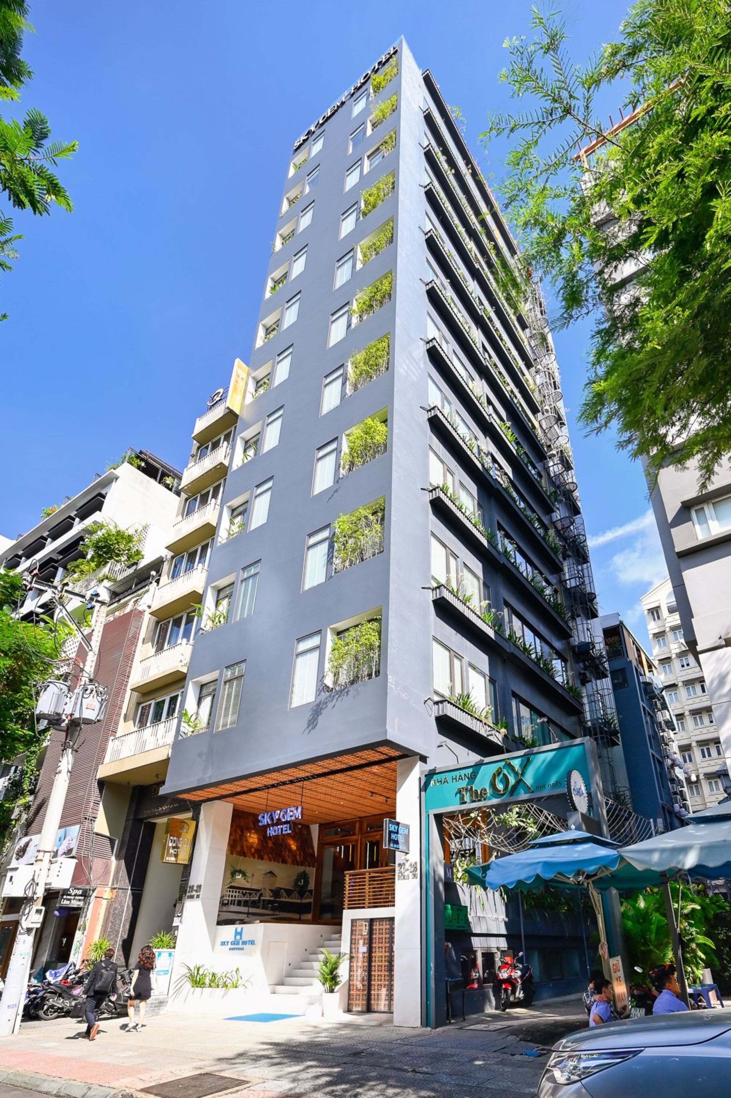 A tall building with multiple balconies, a hotel named "Sky Gem Hotel" at the ground level, and a sign for "The GX" restaurant.