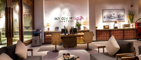 A modern hotel lobby with a reception desk, seating area, and a large window.