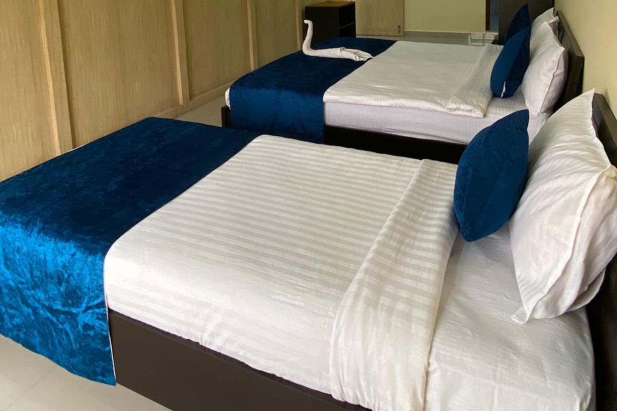 A hotel room with two beds, each with blue and white bedding, a wooden wardrobe, and a mirror on the wall.