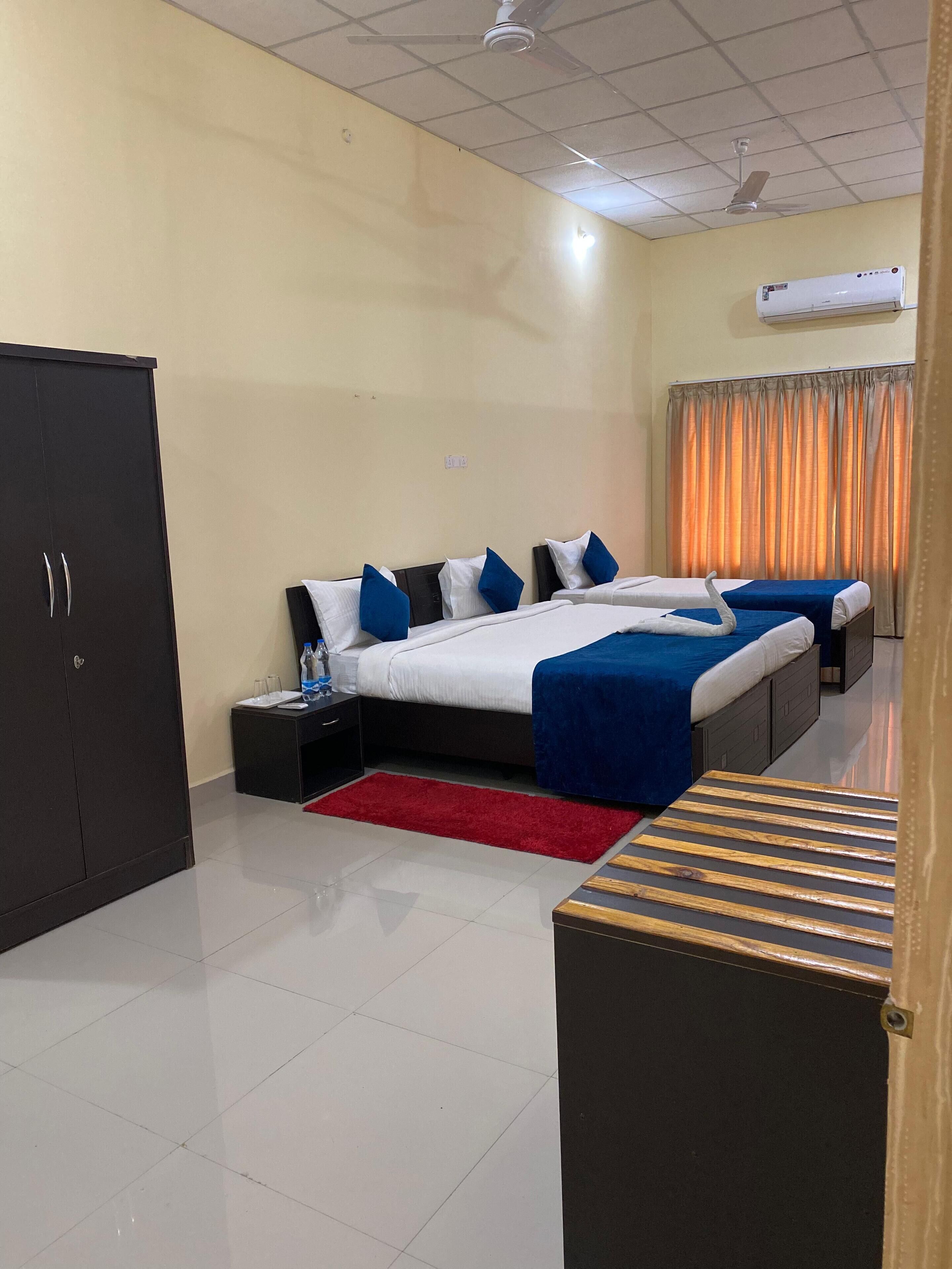 A hotel room with two beds, a wardrobe, a red rug, and an air conditioning unit.