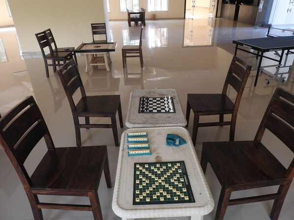 A room with two chess tables, one with a Scrabble board, and several chairs arranged around them.