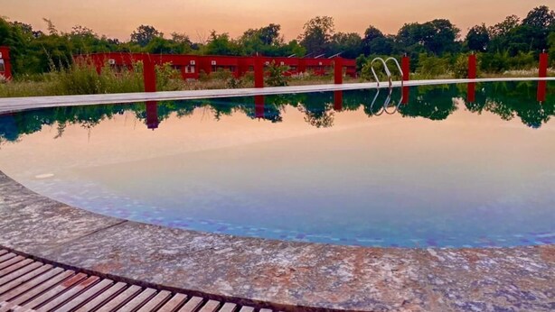 Une piscine aux eaux cristallines, avec une terrasse en bois au premier plan et des structures rouges en arrière-plan.