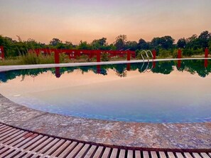 A clear swimming pool with a wooden deck in the foreground and red structures in the background.