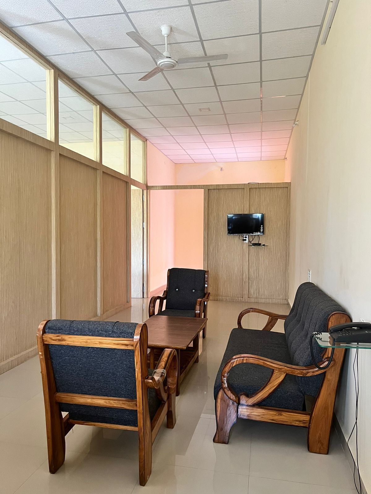 Un salón de conferencias con mobiliario de madera, un ventilador de techo y un televisor montado en la pared.