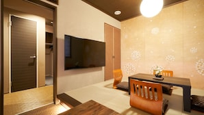 A modern dining area with a wooden table and chairs, a flat-screen TV mounted on the wall, and a decorative wall with a floral pattern. - Private Hotel Kanazawa SHIKI (Kanazawa)