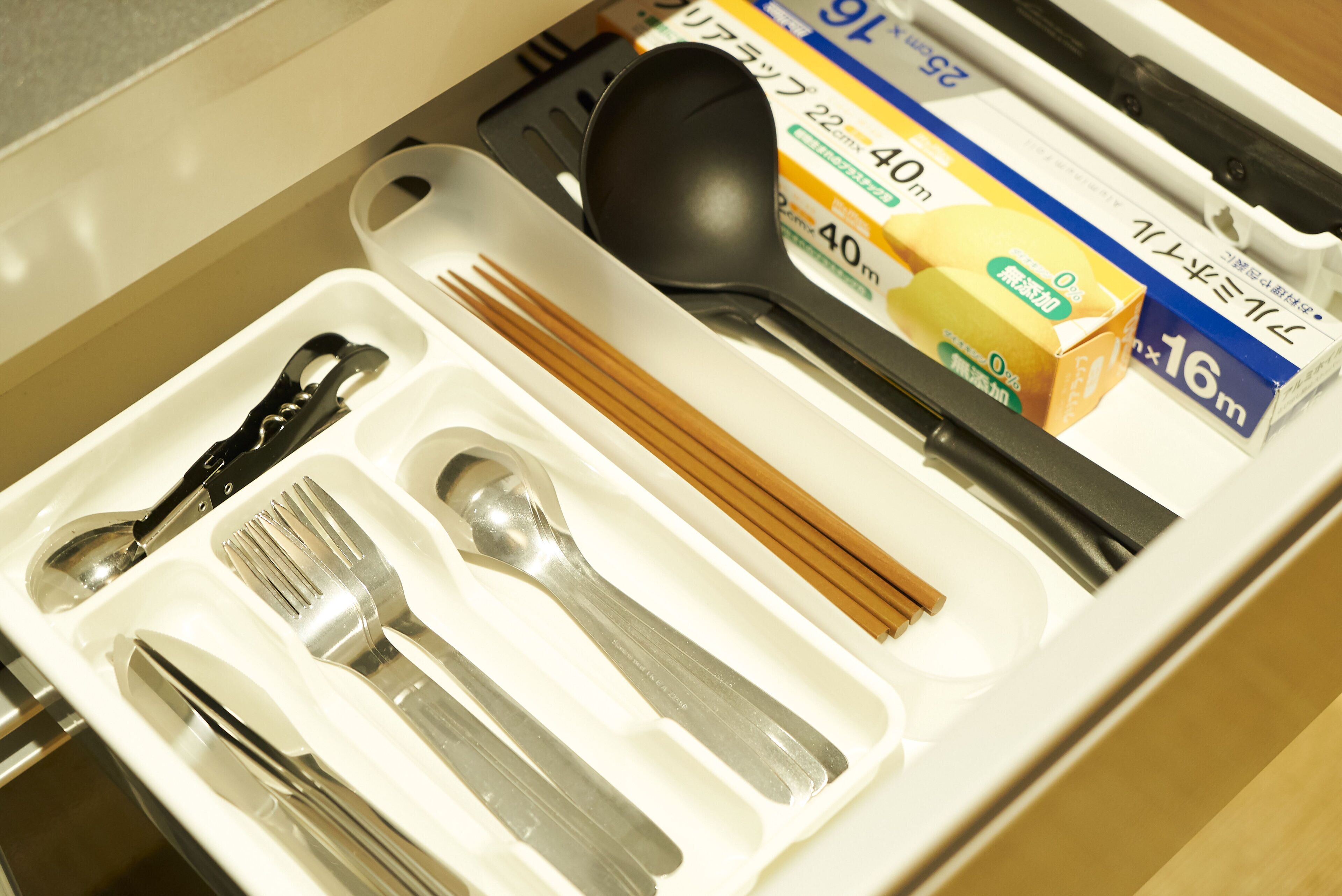 Uma gaveta com talheres organizados, pauzinhos e alimentos embalados.