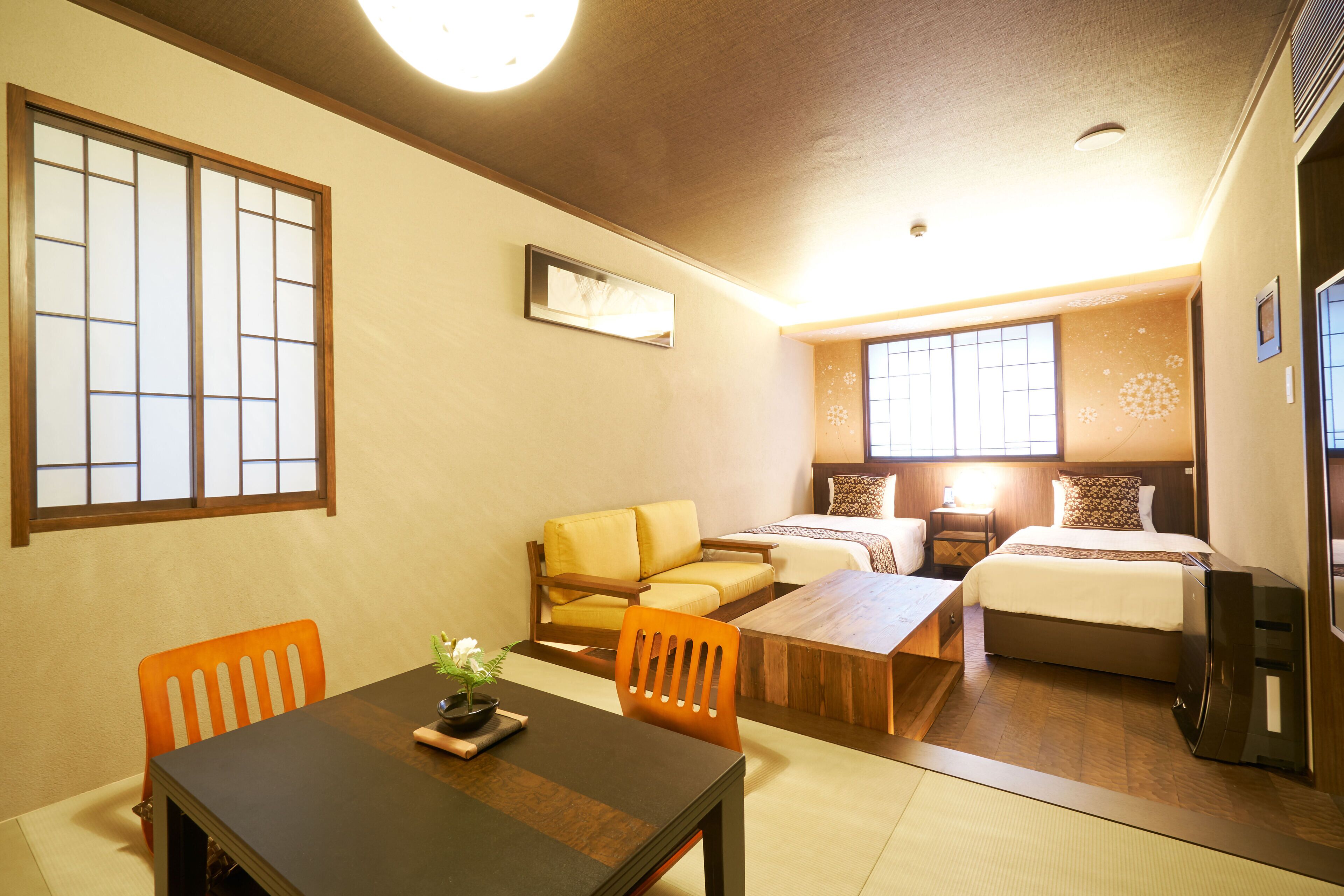 A traditional Japanese-style room with tatami flooring, a low wooden table, a sofa, and a bed with a wooden headboard.