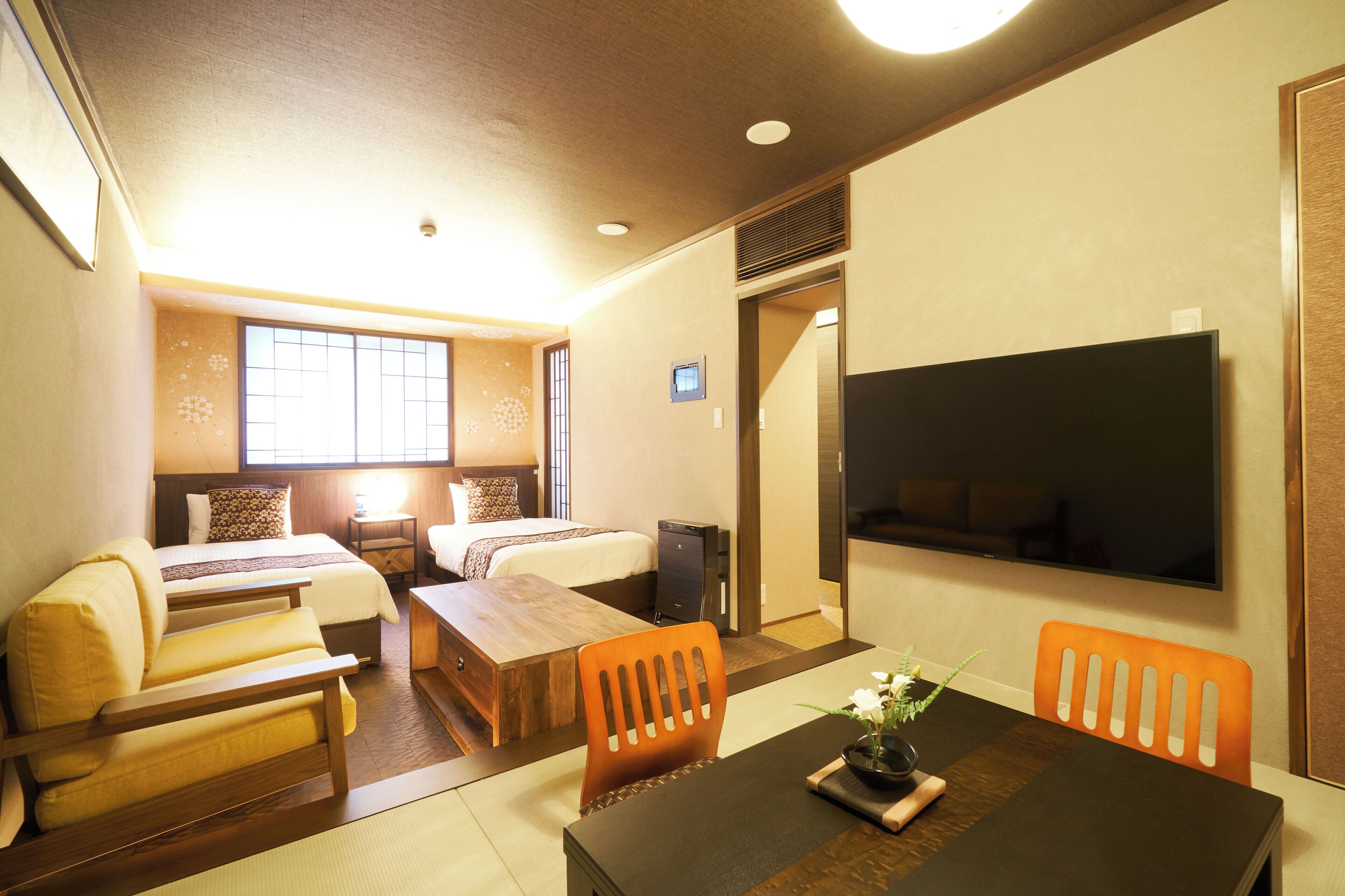 Quarto de hotel com cama, sofá, mesa de jantar, cadeiras e televisão.
