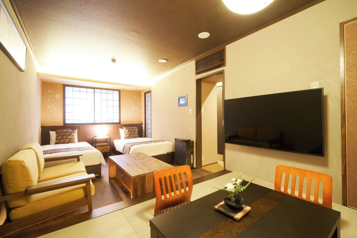 A hotel room with a bed, sofa, dining table, chairs, and a TV.
