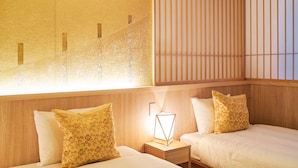 A hotel room with two beds, a nightstand with a lamp, and a window with vertical blinds. - Private Hotel Kanazawa SHIKI (Kanazawa)