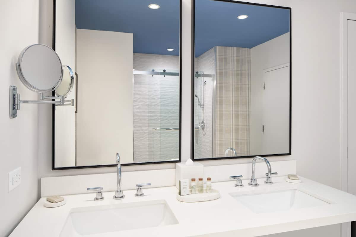 A modern bathroom with two sinks, a large mirror, and a shower area.