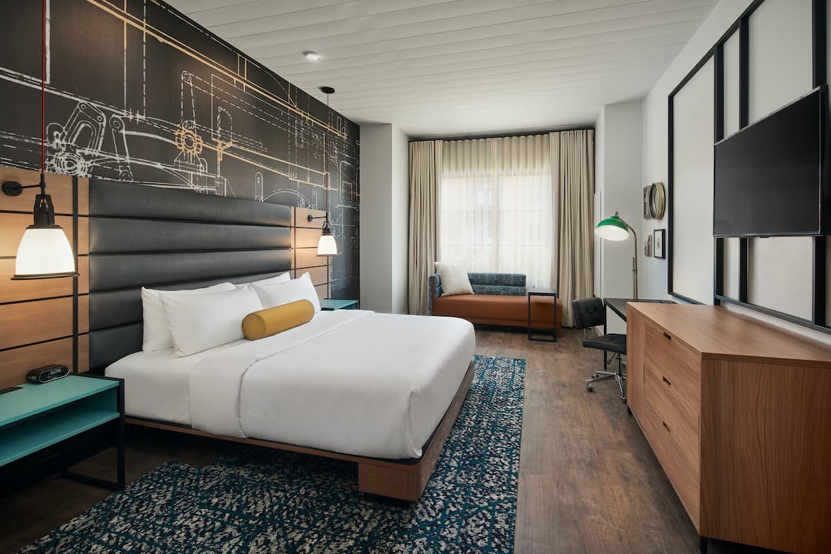 A modern hotel room with a large bed, a desk, a TV, and a window with curtains.