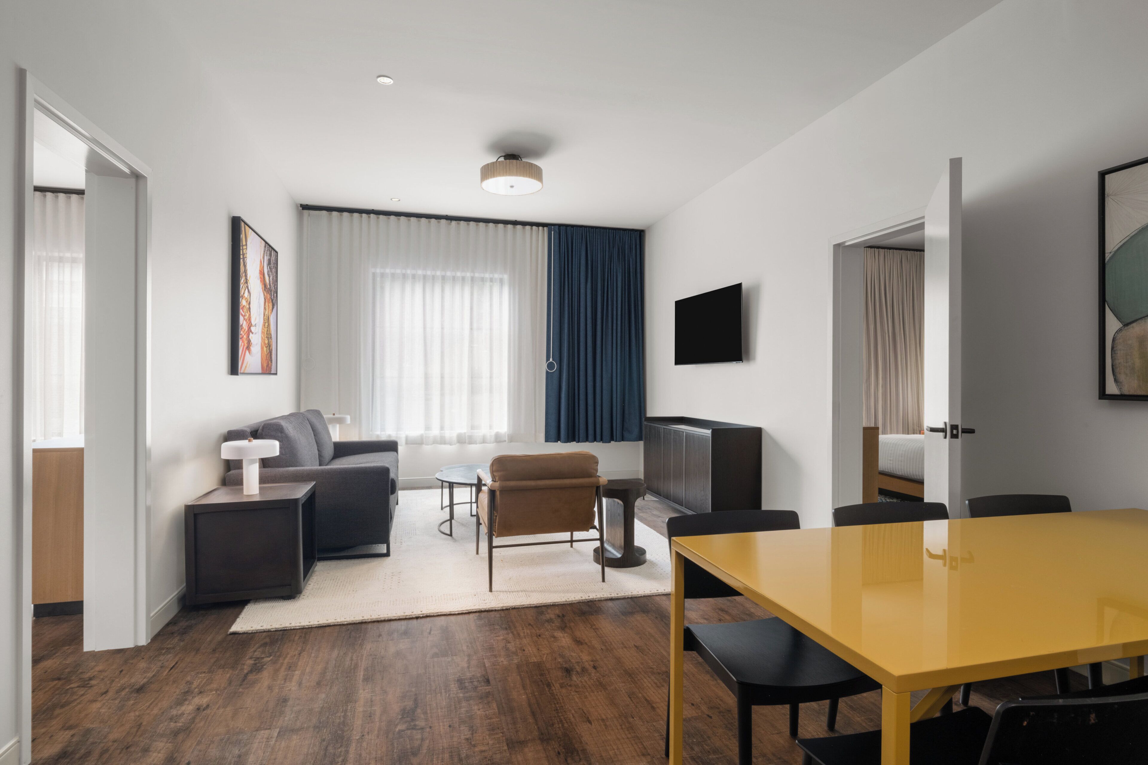 A modern living room with a sofa, a coffee table, a TV, and a dining table with chairs.