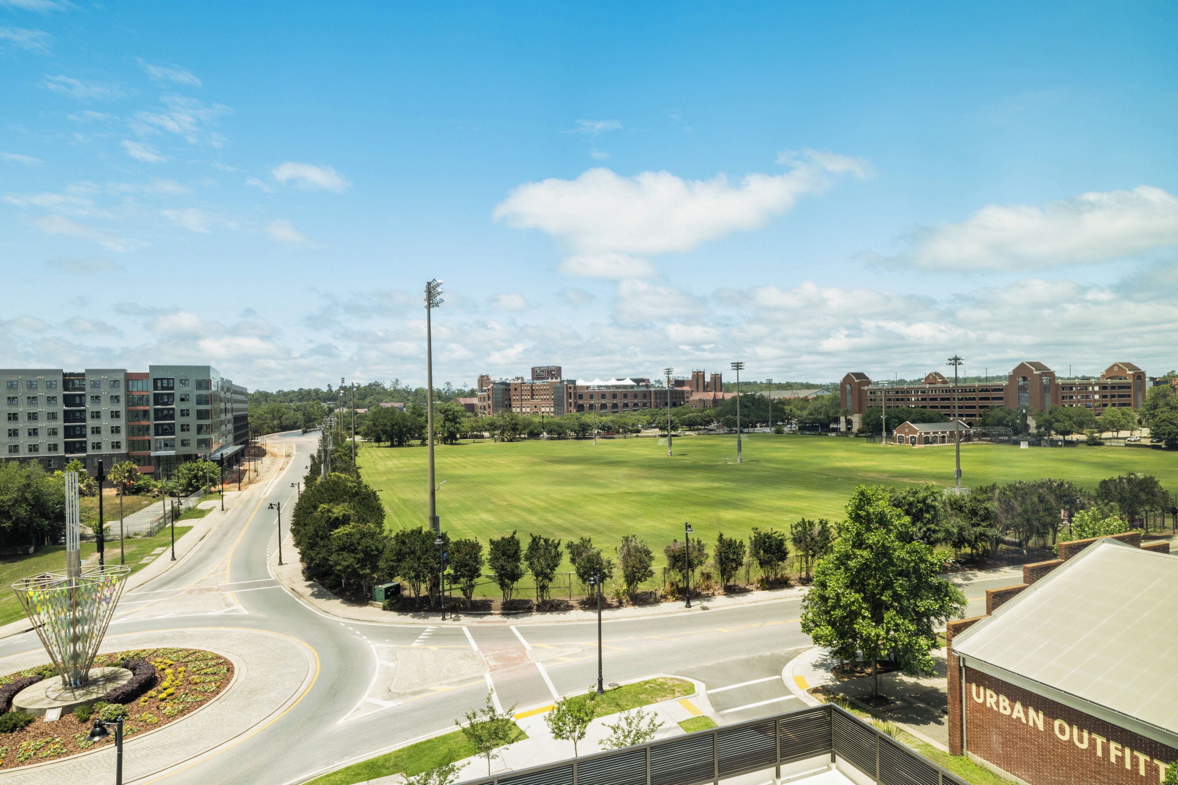 Um campus com um grande campo verde, edifícios e uma estrada com uma rotatória.