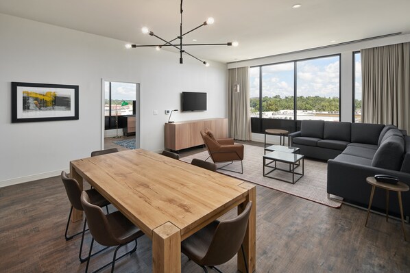 Un moderno salón con una mesa de comedor de madera, un sofá negro y un amplio ventanal con vistas a la ciudad.