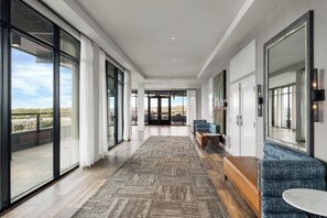 A modern hotel corridor with large windows, a patterned carpet, and seating areas.
