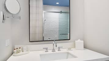 A modern bathroom with a large mirror, a white sink, and a glass shower enclosure.