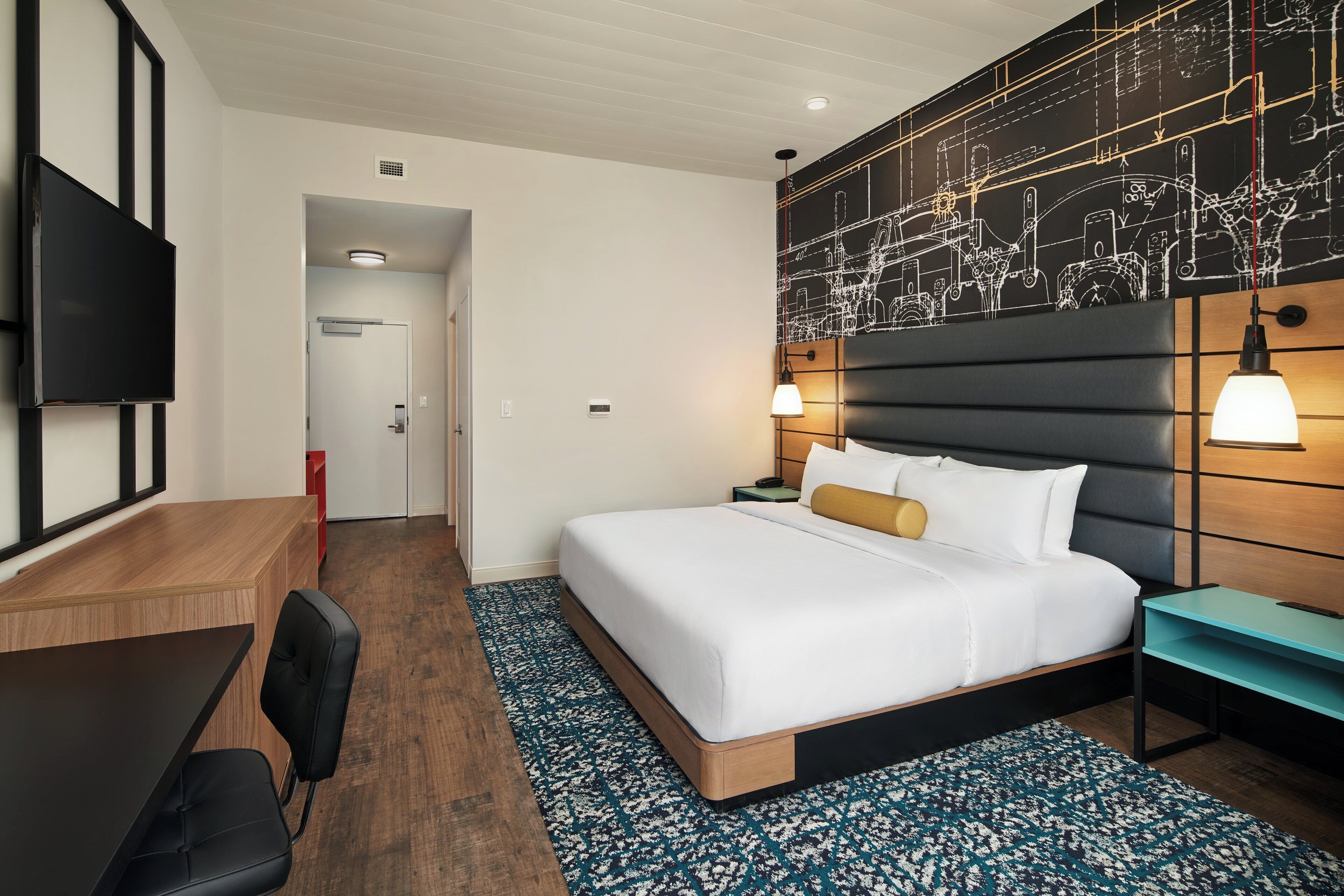 Ein Hotelzimmer mit einem Bett, einem Schreibtisch, einem Stuhl, einem Fernseher und einer Wand mit einem Bauplan-Design.