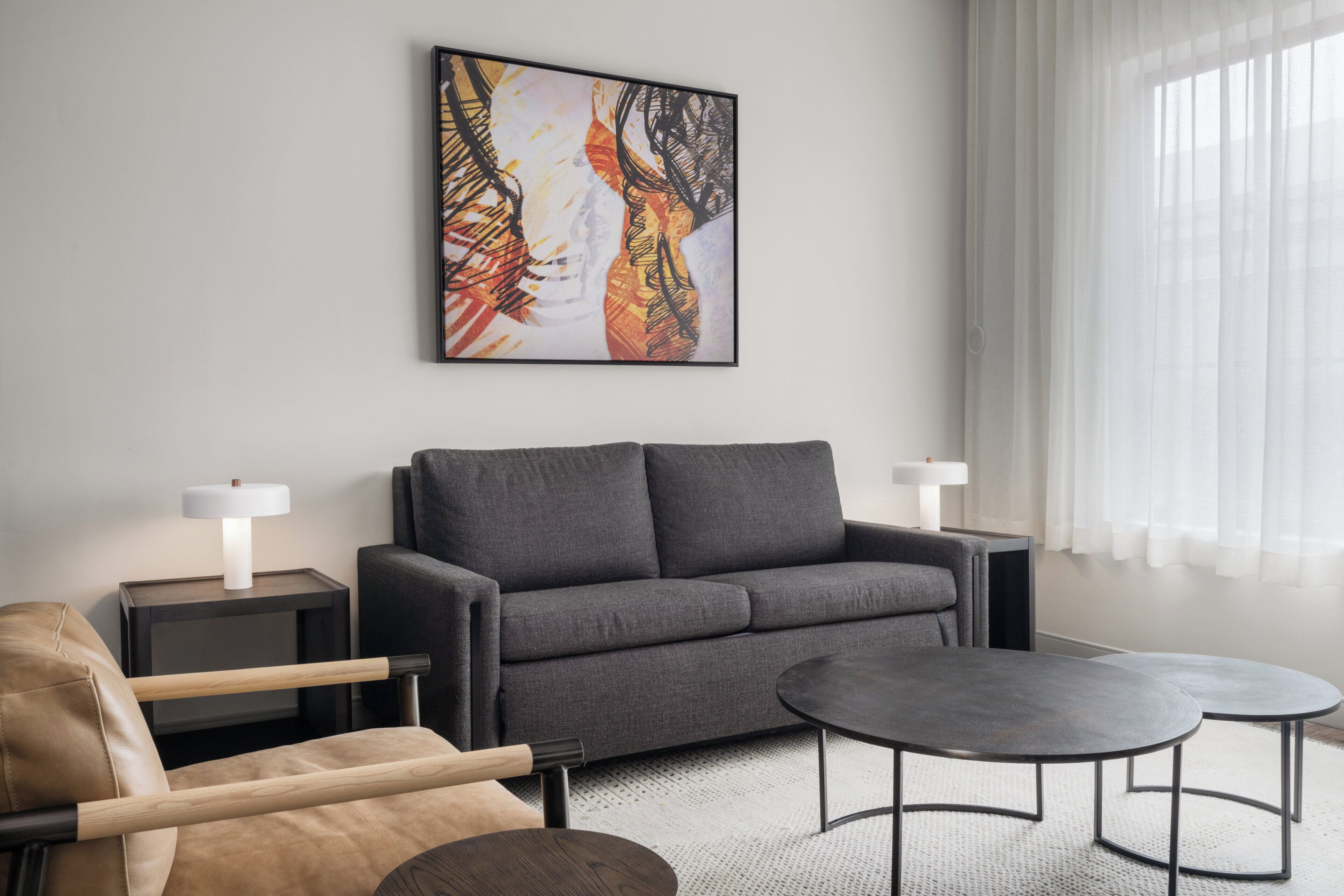 A modern living room with a gray sofa, two side tables with lamps, a round coffee table, and a beige armchair.