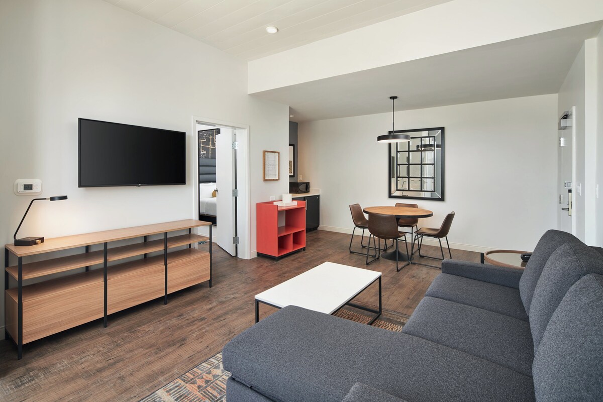 A modern living room with a flat-screen TV, a sofa, a coffee table, and a dining area with a table and chairs.