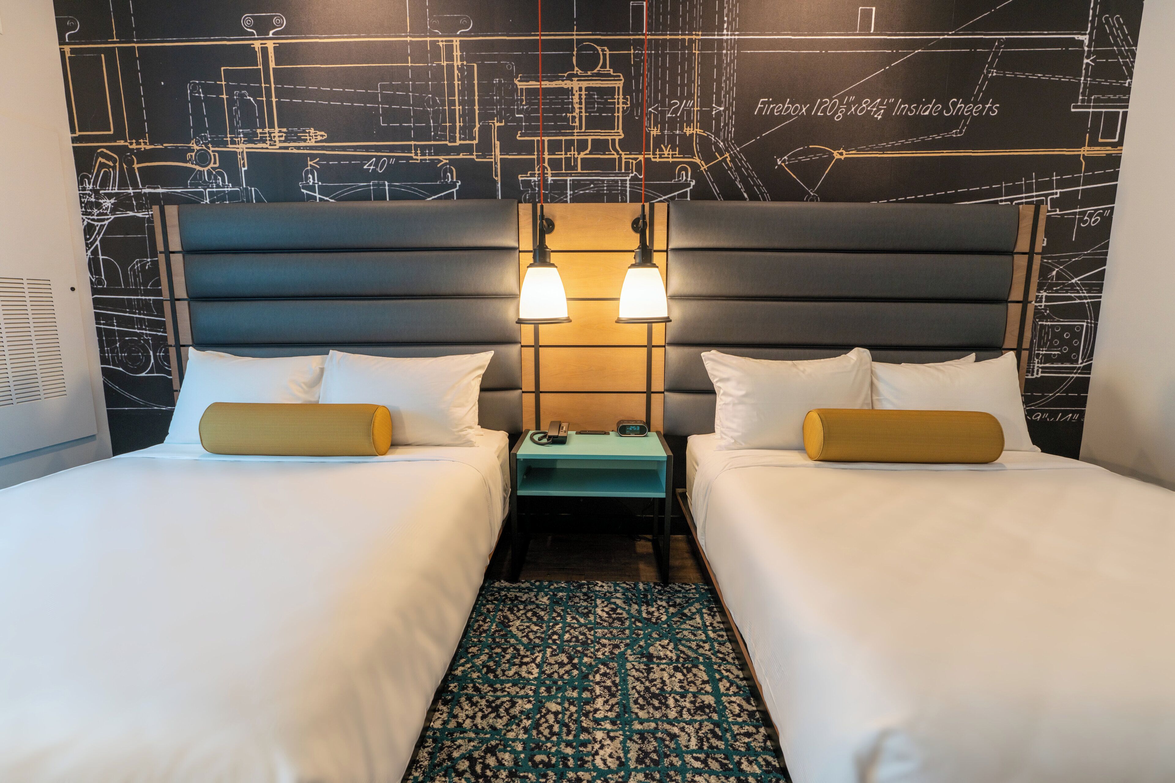Et hotelværelse med to senge, et tæppe med mønster og en væg med et plantegningsdesign.