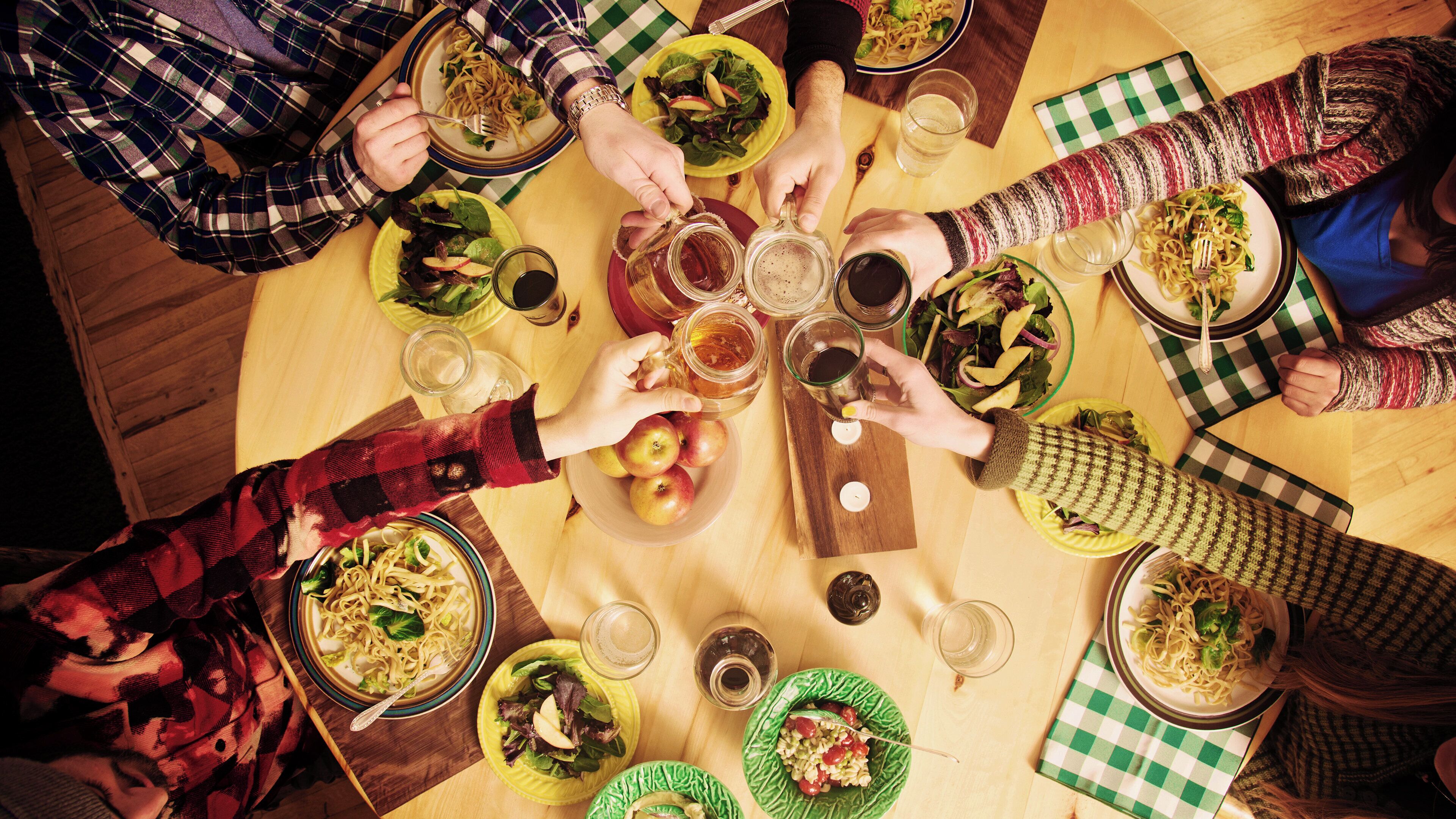 Un groupe de personnes est réuni autour d’une table, où l’on voit divers plats et boissons, ce qui suggère un moment de convivialité ou un repas partagé.