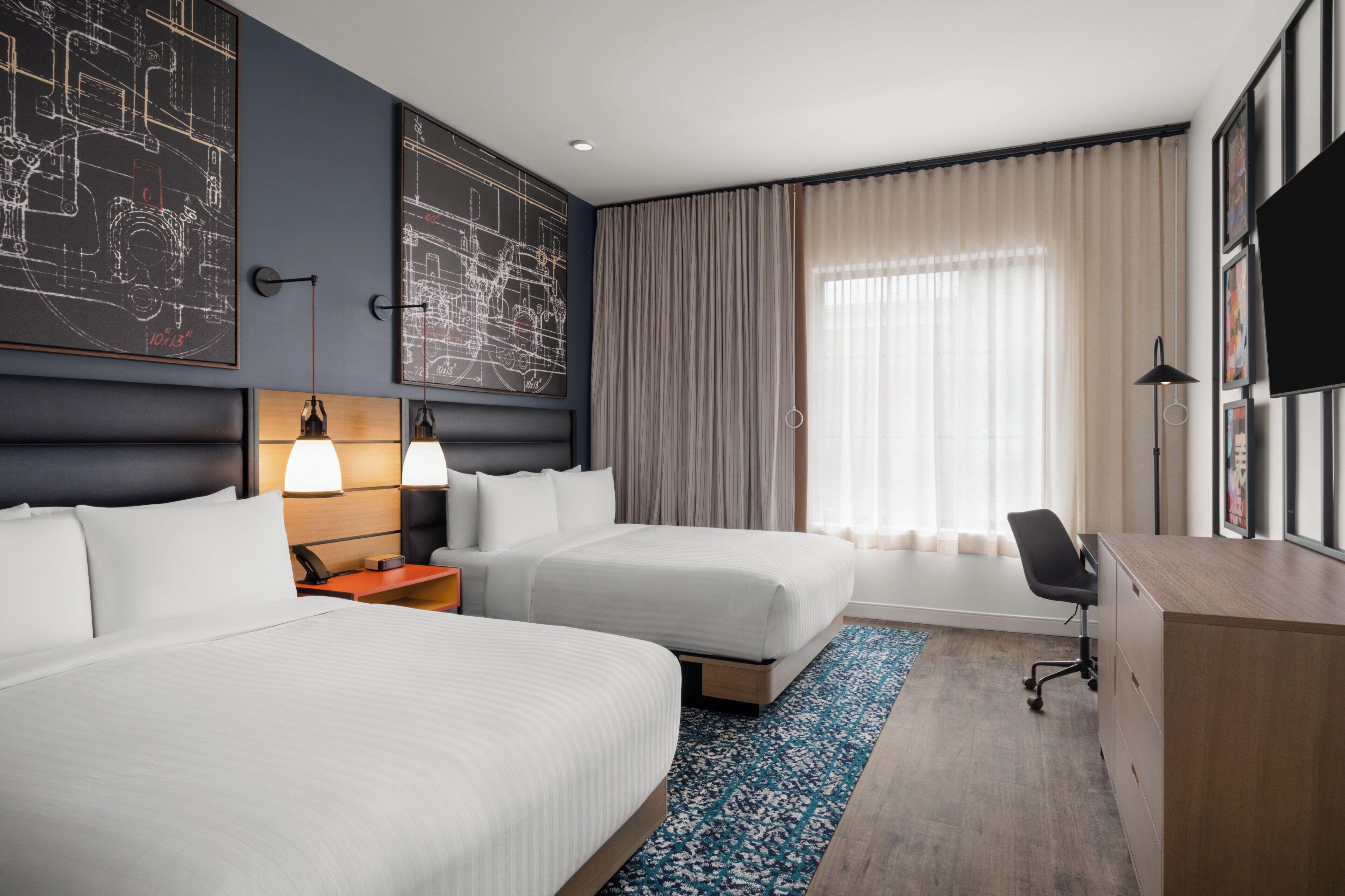 Ett hotellrum med två sängar, ett skrivbord, en stol, en TV och ett stort fönster med gardiner.