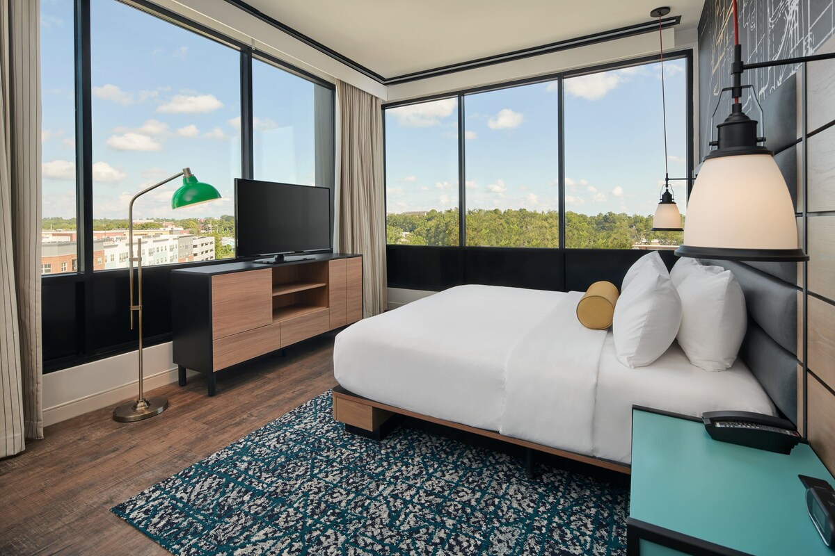 Una habitación de hotel moderna con una cama grande, televisión, escritorio y vistas a la ciudad.