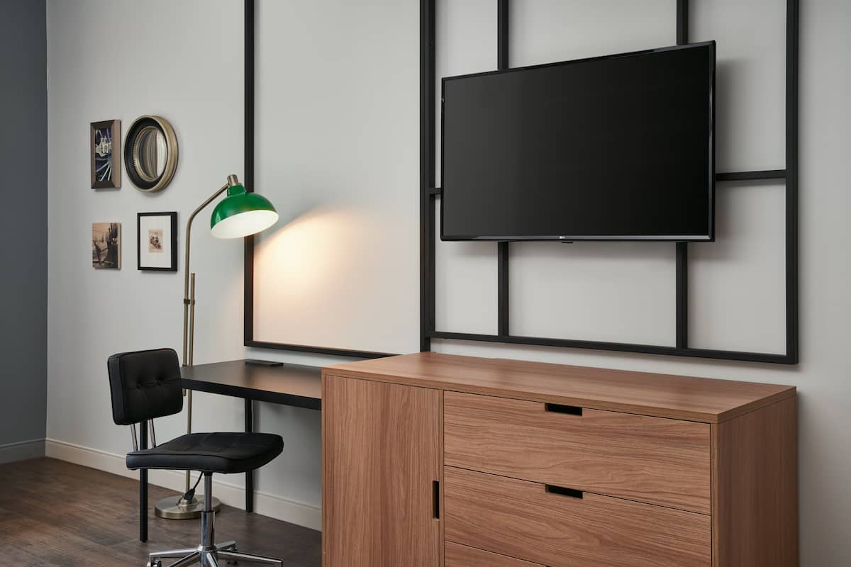 A modern room with a wooden desk, a black office chair, a green desk lamp, and a mounted TV on the wall.